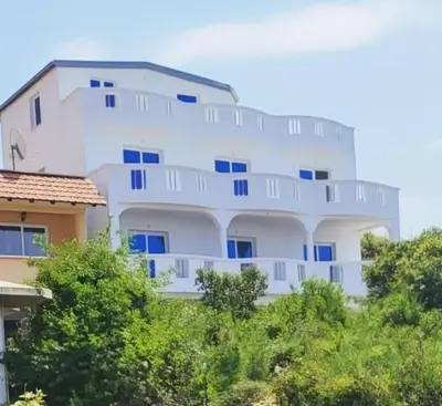 a large white building with blue windows and trees at Hotel Kunjui in Utjeha