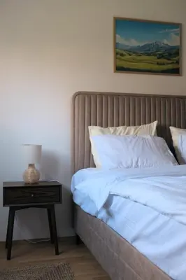 a bed with white sheets and a nightstand with a lamp at Olivers Cozy and Spacious Apt in Podgorica