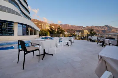 a patio with white tables and chairs and mountains at Skyline Sunset in Becici