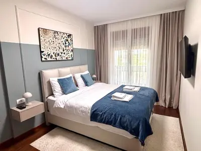 a bedroom with a bed with blue sheets and a window at A&T Lux in Podgorica