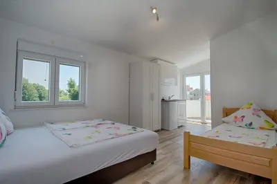 a white bedroom with two beds and two windows at Biševo Apartmani in Donji Štoj
