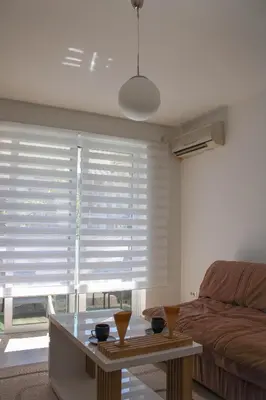 a living room with a window with white blinds at Budva Apartmani in Budva