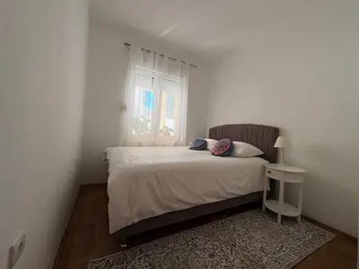 a white bedroom with a bed and a window at Apartman Sunce in Podgorica