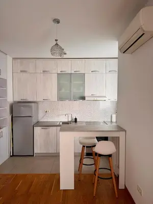 a kitchen with white cabinets and a counter and stools at Bright & Modern Apartment in City Kvart in Podgorica