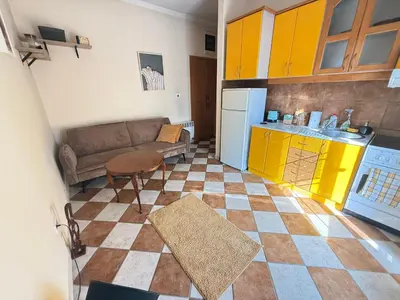 a living room with a couch and a kitchen with yellow cabinets at Charming terrace studio in Podgorica