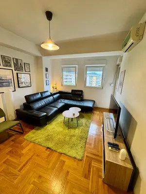 a living room with a black leather couch and a table at Bright & Cozy Urban Apartment in Podgorica