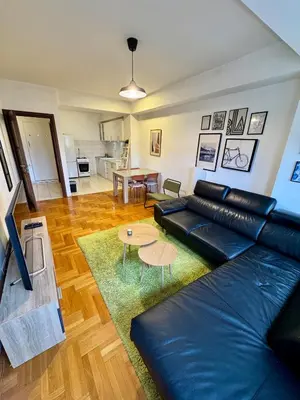 a living room with a black leather couch and a table at Bright & Cozy Urban Apartment in Podgorica