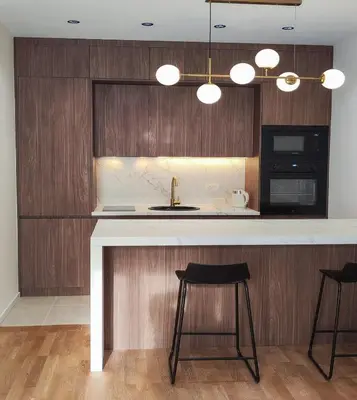 a kitchen with wooden cabinets and a counter with stools at Stylish City Living Elegant One Bedroom Apartment in Podgorica