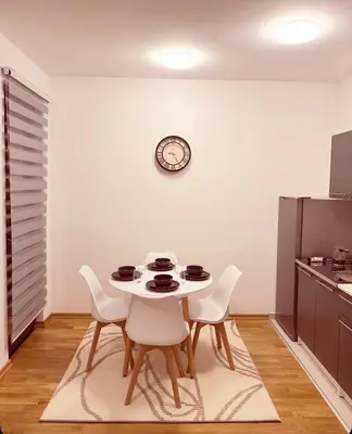a table and chairs in a kitchen with a clock on the wall at Apartman 2937 in Podgorica