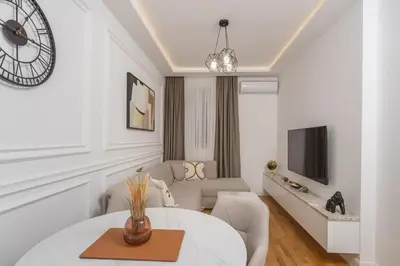 a white living room with a table and a clock at Deluxe Apartment Zarah in Bar