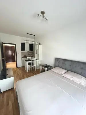 a bedroom with a large white bed and a kitchen at Urban studio City kvart in Podgorica