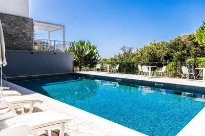 a swimming pool with white chairs and a house at Val Apartment, Przno in Budva