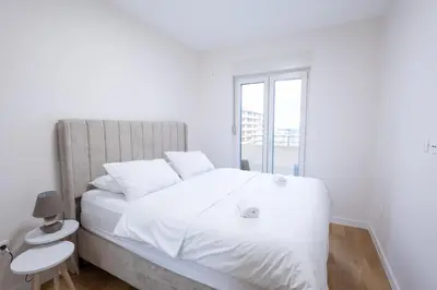 a white bedroom with a large white bed with a window at Urban Stay - Central Point Apartment in Kruševac