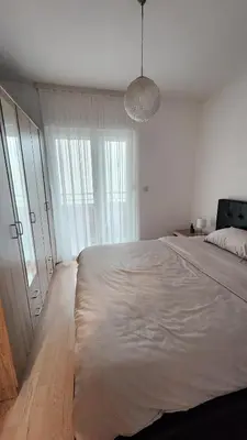a white bedroom with a large bed and a chandelier at Central Light Apartment in Podgorica