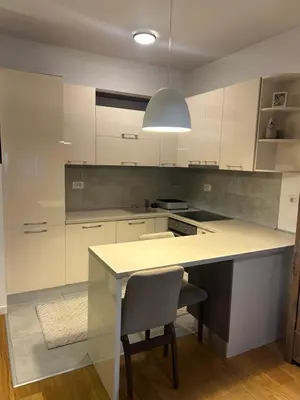 a kitchen with white cabinets and a table and a chair at Apartmani Masa in Podgorica