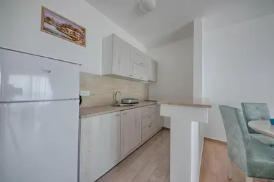 a white kitchen with a refrigerator and a table at Mir i More in Dobra Voda