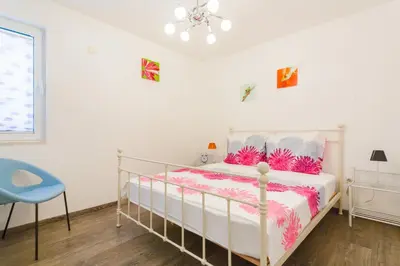 a white bedroom with a bed and a blue chair at Apartment Mia in Sveti Stefan