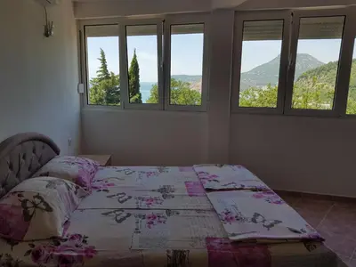 a bedroom with a bed with a quilt and three windows at Guest House Dragomir in Sutomore