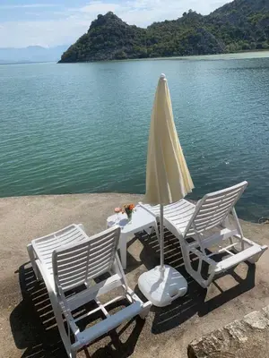 two chairs and a table with an umbrella next to the water at Holiday home Raduš in Virpazar