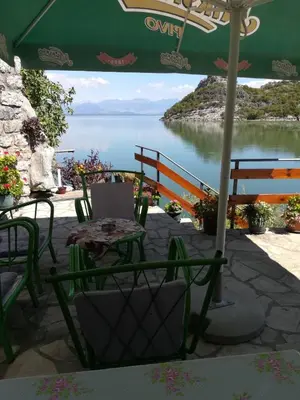 a table and chairs under an umbrella with a view of a lake at Holiday home Raduš in Virpazar