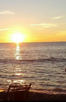 a sun setting over the ocean with a beach chair at Apartmani Vukmanovic in Čanj