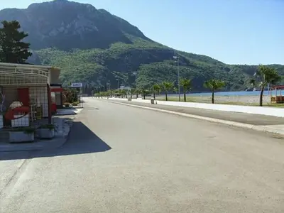 an empty street next to a lake and a mountain at Apartmani Vukmanovic in Čanj