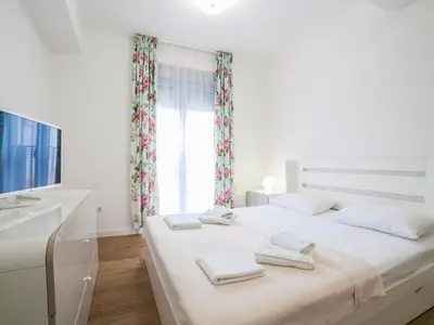 a white bedroom with a large bed and a window at Apartments My Przno in Sveti Stefan