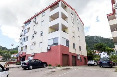 a white and red building with cars parked in a parking lot at Apartment Natasha in Budva
