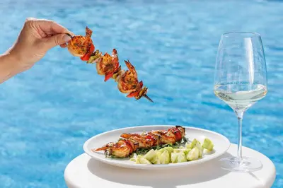 a plate of food with shrimp and a glass of wine at Dukley Hotel & Resort in Budva