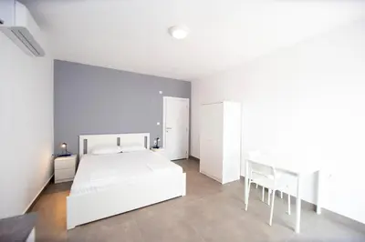 a white bedroom with a white bed and a chair at Apartments Mika in Budva