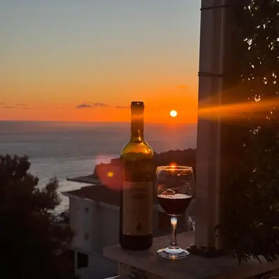 a bottle of wine and a glass on a balcony with the sunset at Apartman Aleksandar in Ulcinj