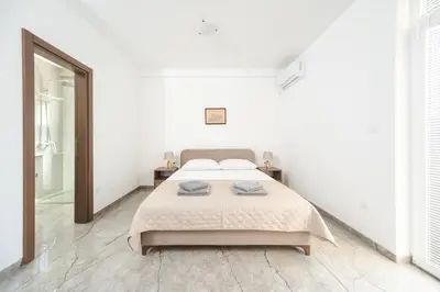 a white bedroom with a bed and a mirror at Apartmani Agape in Petrovac na Moru