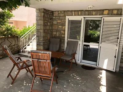 a patio with two chairs and a wooden table and chairs at Three Palms Apartments Novakovic in Petrovac na Moru