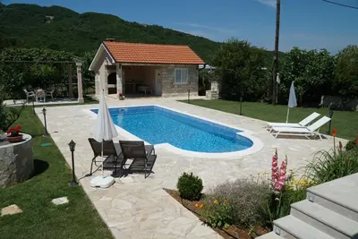 a swimming pool with chairs and a house at Apartments Raskovic in Radanovići