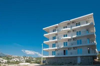 a tall white building with balconies and a blue sky at Open Sea Apartments in Utjeha