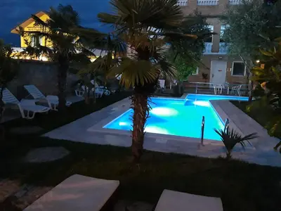 a pool with a palm tree next to a building at Kazablanka Rooms Aerodrom in Podgorica