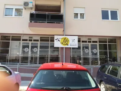 a red car parked in front of a building with a sign at Apartment S&S Budva in Budva