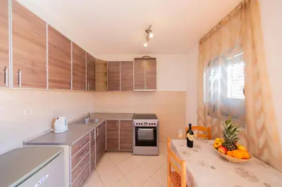 a kitchen with wooden cabinets and a table with a bowl of fruit at SMS Apartments in Budva