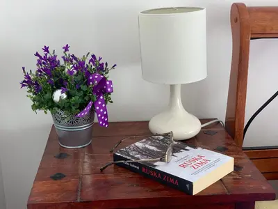 a table with a book and a lamp and a vase of flowers at Karina Apartment in Budva