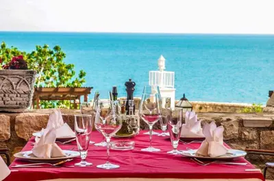 a table with wine glasses and napkins and the ocean at Villa Marinero in Ulcinj