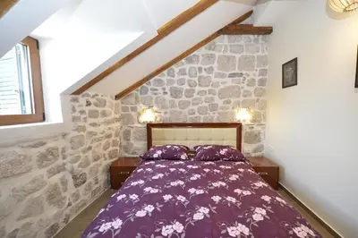 a bedroom with a purple bed in a stone wall at Palazzo Max and Alex Apartments in Kotor