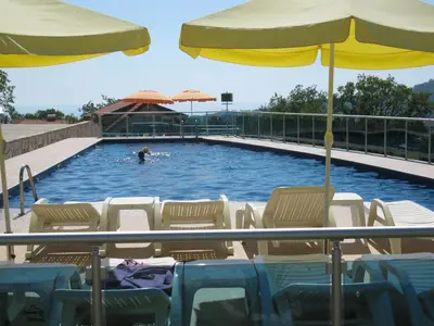 a person swimming in a pool with chairs and an umbrella at Zubci mountain apartment in Bar