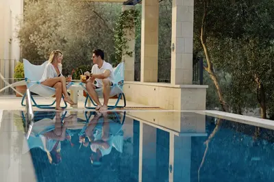 a man and woman sitting at a table next to a pool at Hotel Eleven in Petrovac na Moru