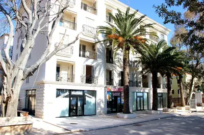 a white building with palm trees in front of it at Vasiliki Seaside Apartments in Petrovac na Moru