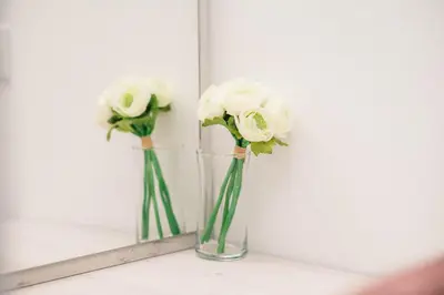 two white roses in a vase in a mirror at Apartments Antique in Ulcinj
