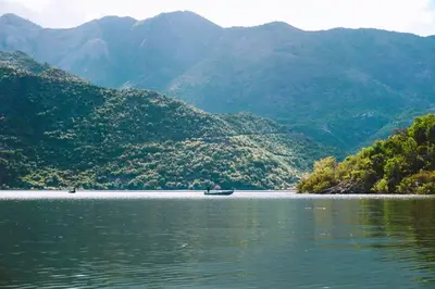 a boat in the middle of a lake with mountains at Apartmani Konoba Starčevo in Virpazar