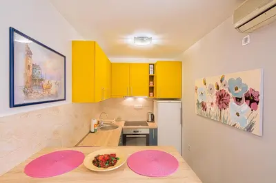 a kitchen with yellow cabinets and pink plates on a table at Apartman Aleksandra in Budva