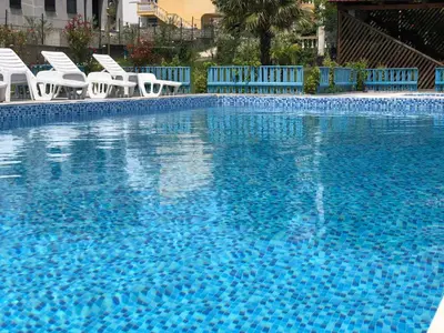 a large blue swimming pool with white chairs in it at Guest House Green Garden in Ulcinj