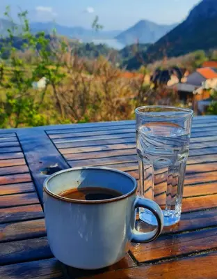 a cup of coffee and a glass of water on a table at Dembelija Rooms in Virpazar