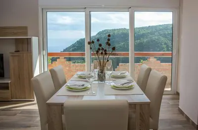 a dining room table with chairs and a large window at Apartments Bonaca in Budva